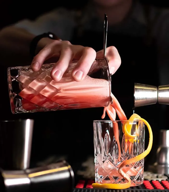 Ein rosafarbener Cocktail wird aus einem Kristallkrug in ein Glas gegossen