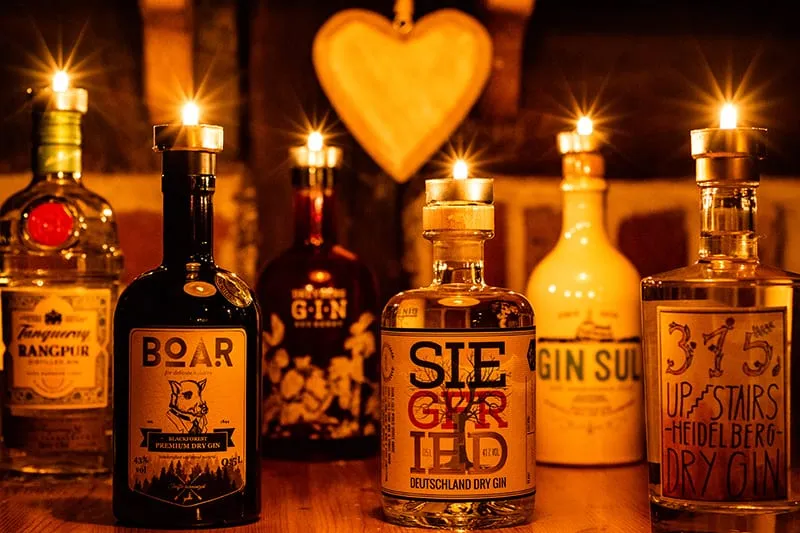 Vier Gin-Flaschen mit brennenden Kerzen auf dem Verschluss, dahinter ein leuchtendes Herz