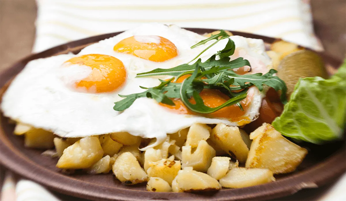 Bratkartoffeln mit Spiegeleiern und Rucola auf einem Teller