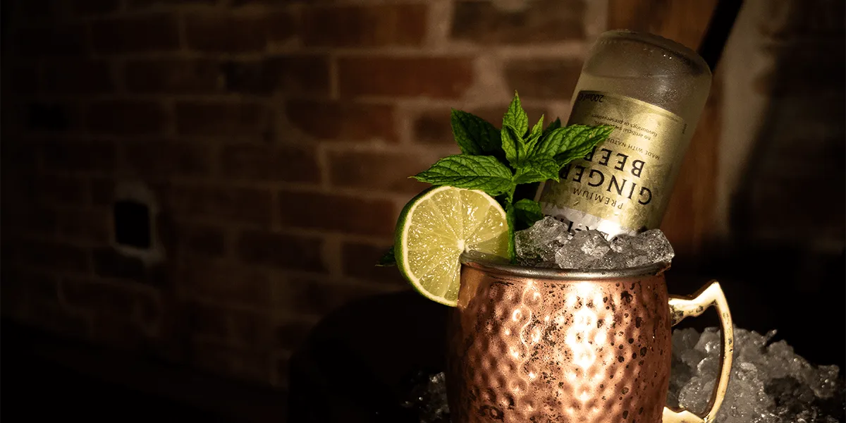 Moscow Mule im Kupferbecher mit Limette und Minze vor einer Ziegelwand