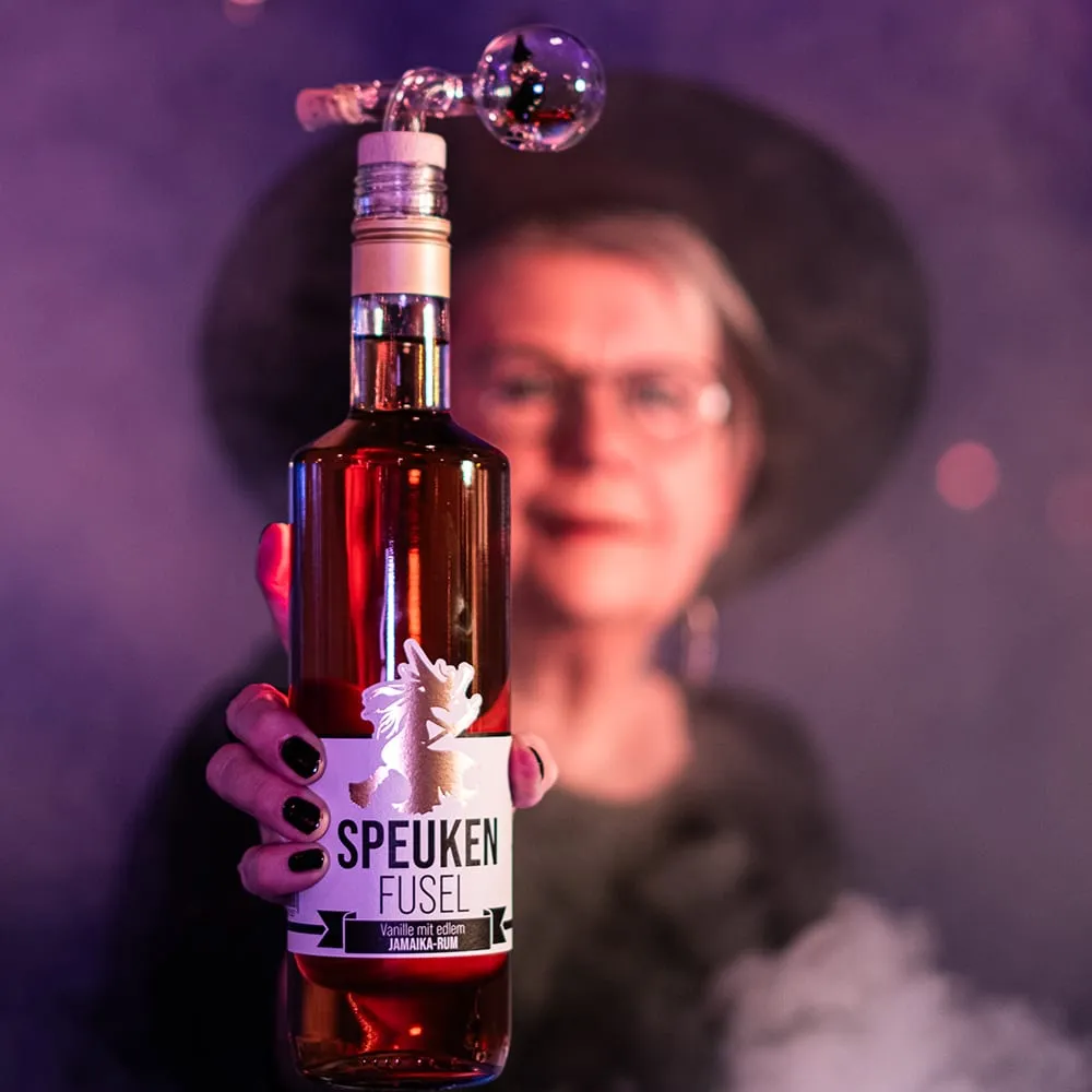 Flasche „Speuken Fusel“ mit Hexenetikett vor lila Nebel