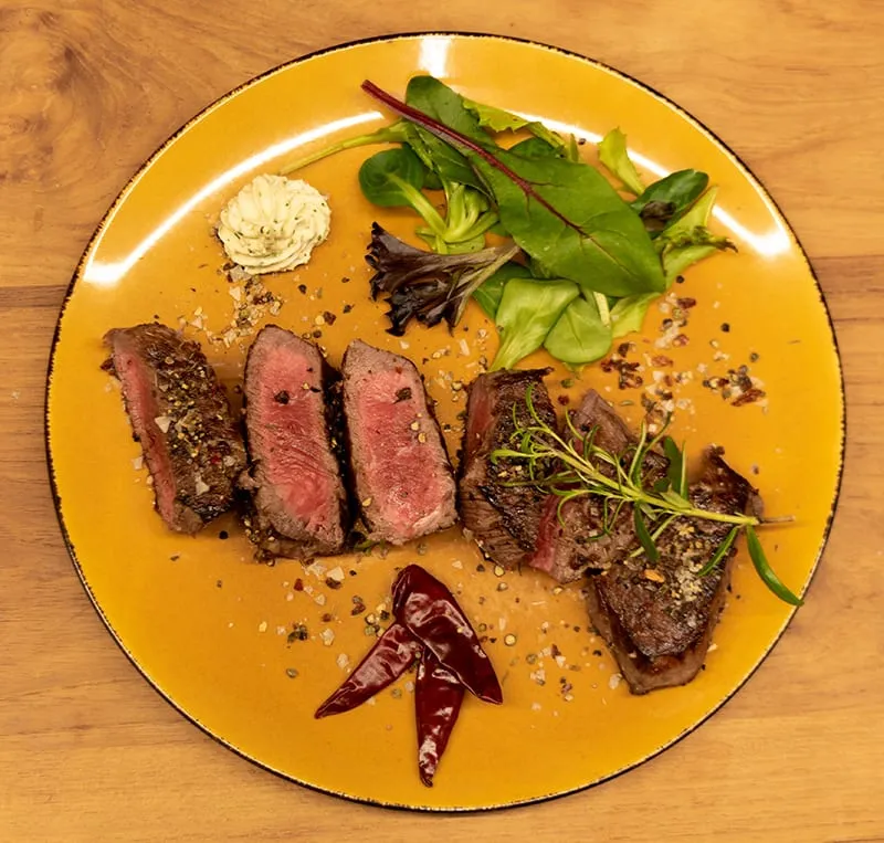 Aufgeschnittenes, rosa gebratenes Steak auf einem Teller mit Salat und Kräuterbutter